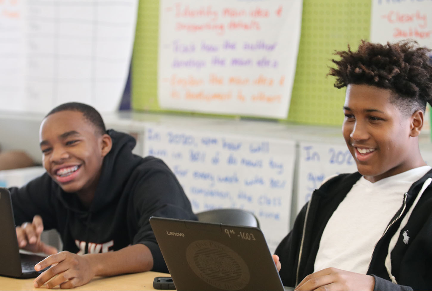 Two male students smiling while using laptops